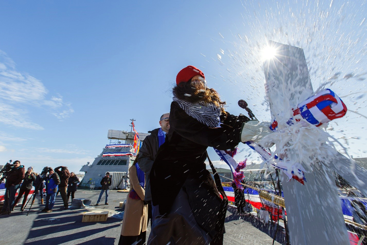 Ship sponsor Alba Tull christens LCS 23 by smashing a champagne bottle across the hull in a ceremony officially naming the ship “Cooperstown.” Credit: Lockheed Martin.